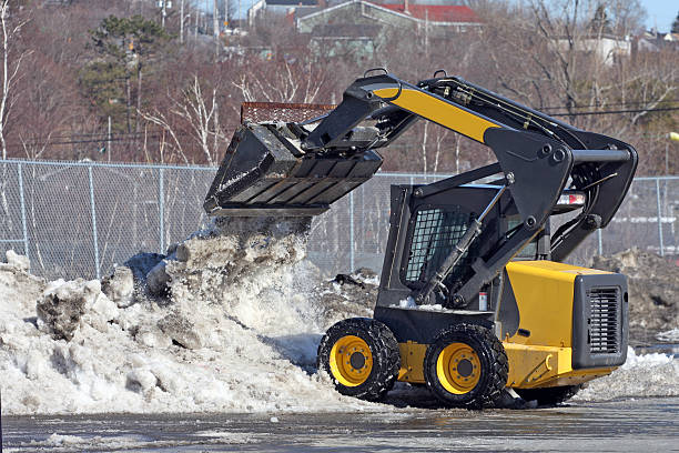 Mini front end loader removes snow from a mall parking lot.